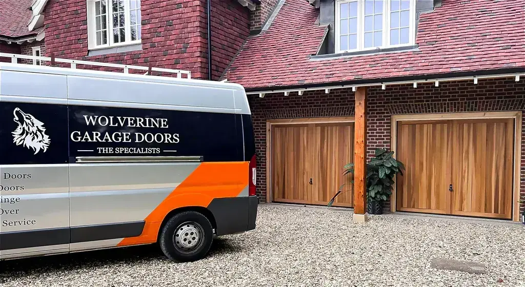 A Wolverine Garage Doors van parked on a driveway beside two new timber garage doors
