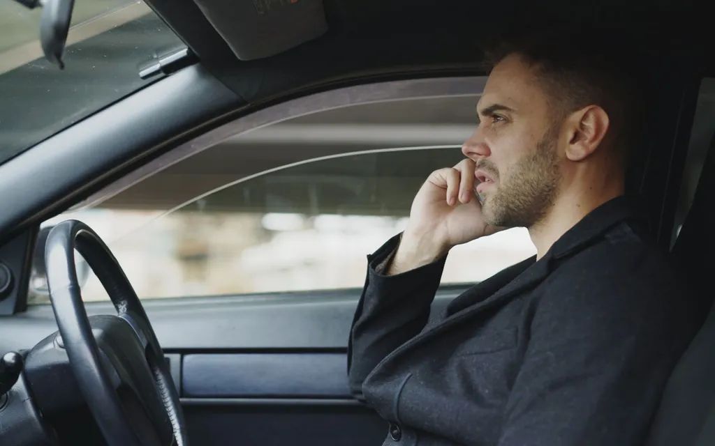 Driving instructor in the driver&rsquo;s seat of a car taking a call on his phone